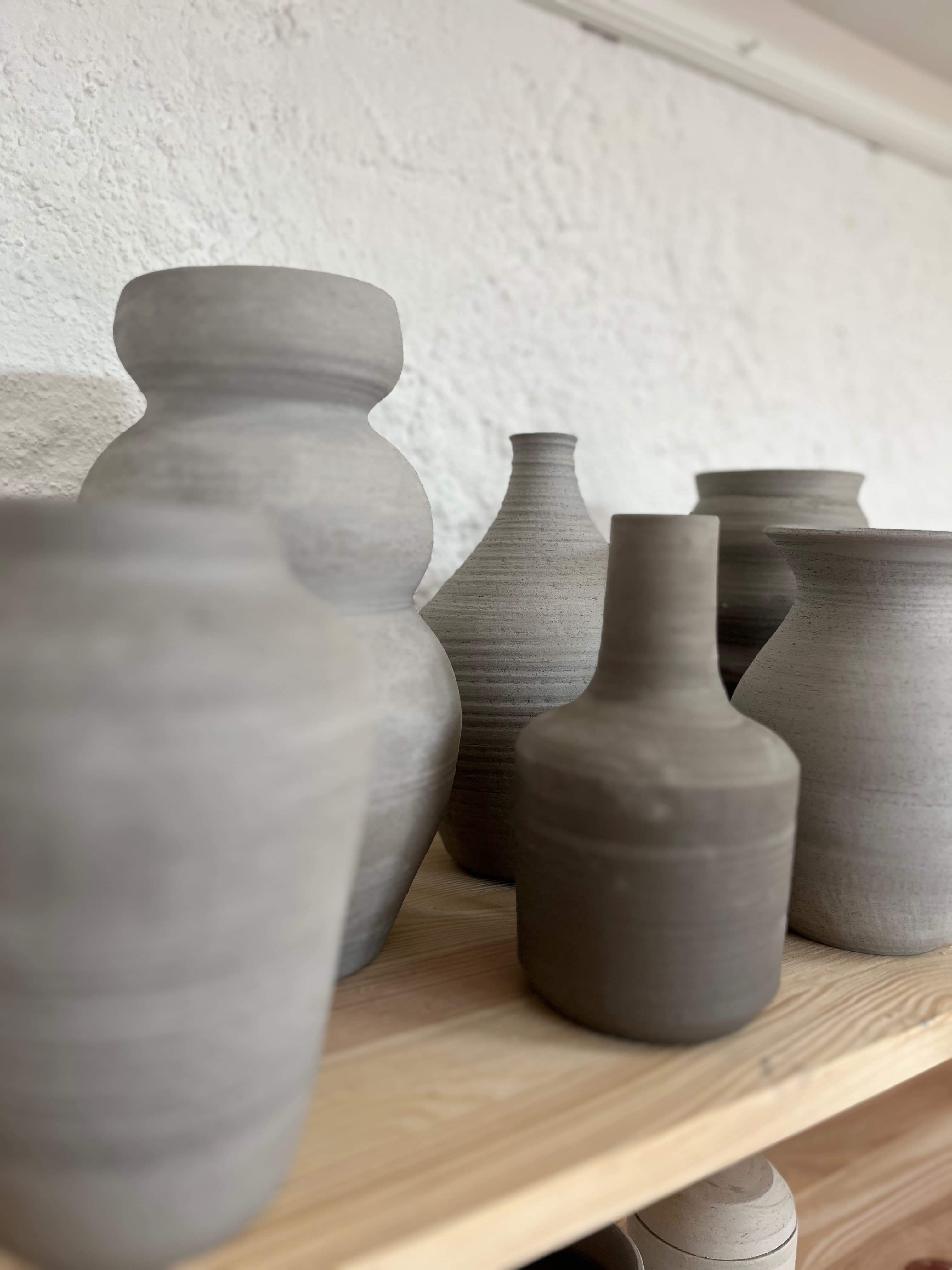 Hand-thrown grey clay vessels on a wooden shelf